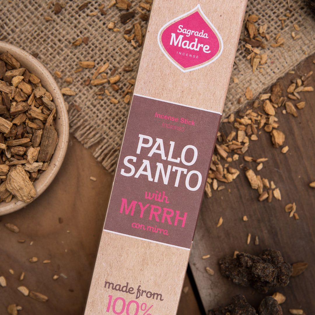 Sagrada Madre Palo Santo with Myrrh packaging on a rustic background with scattered Palo Santo sticks.