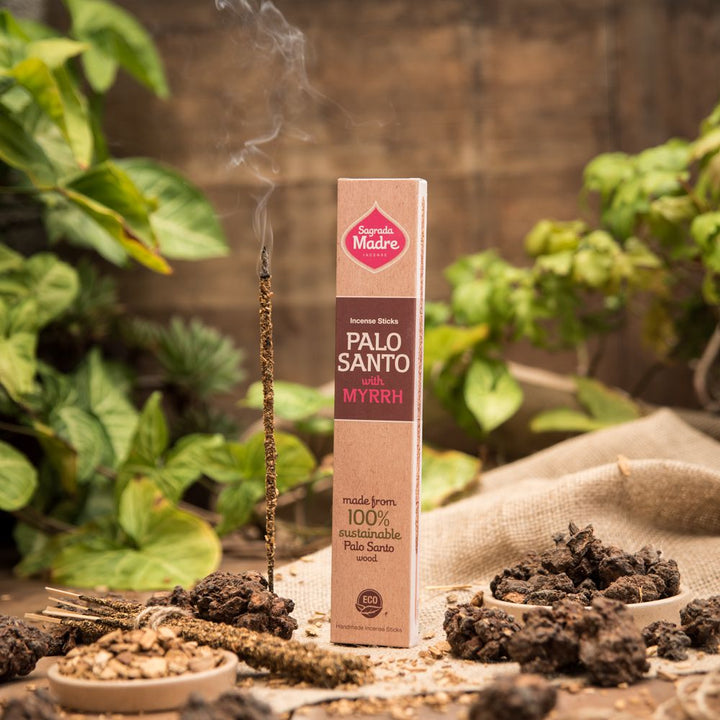 A box of Sagrada Madre Palo Santo incense sticks with myrrh, surrounded by natural elements and incense smoke rising in the background.