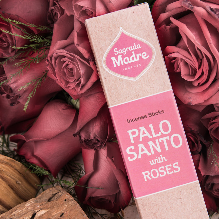Box of Sagrada Madre Palo Santo with Roses incense sticks surrounded by pink roses.