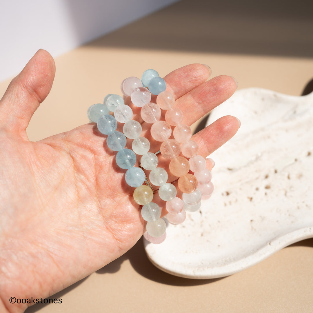Natural Morganite bracelet with soft pastel pink, peach, aqua and champagne beryl beads from Brazil displayed in hand and on a stone tray.