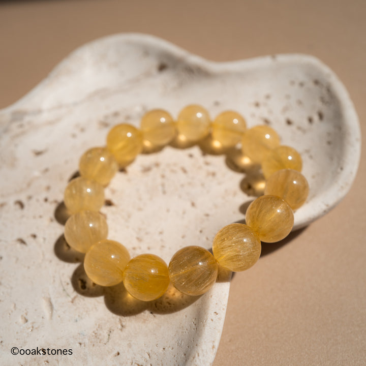 Natural Yellow Fluorite bracelet with transparent golden beads from Inner Mongolia displayed on a natural stone dish.