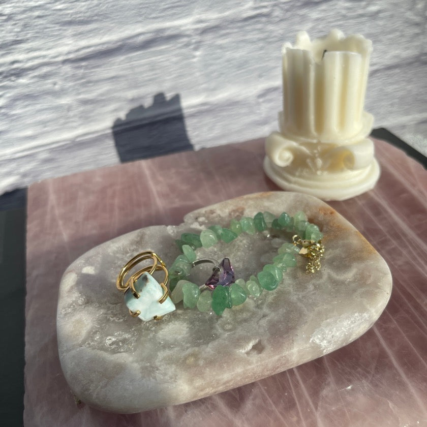 Lilac purple color pink amethyst jewelry dish with crystal ring and bracelet in it styled on top of a rose quartz slab and candle